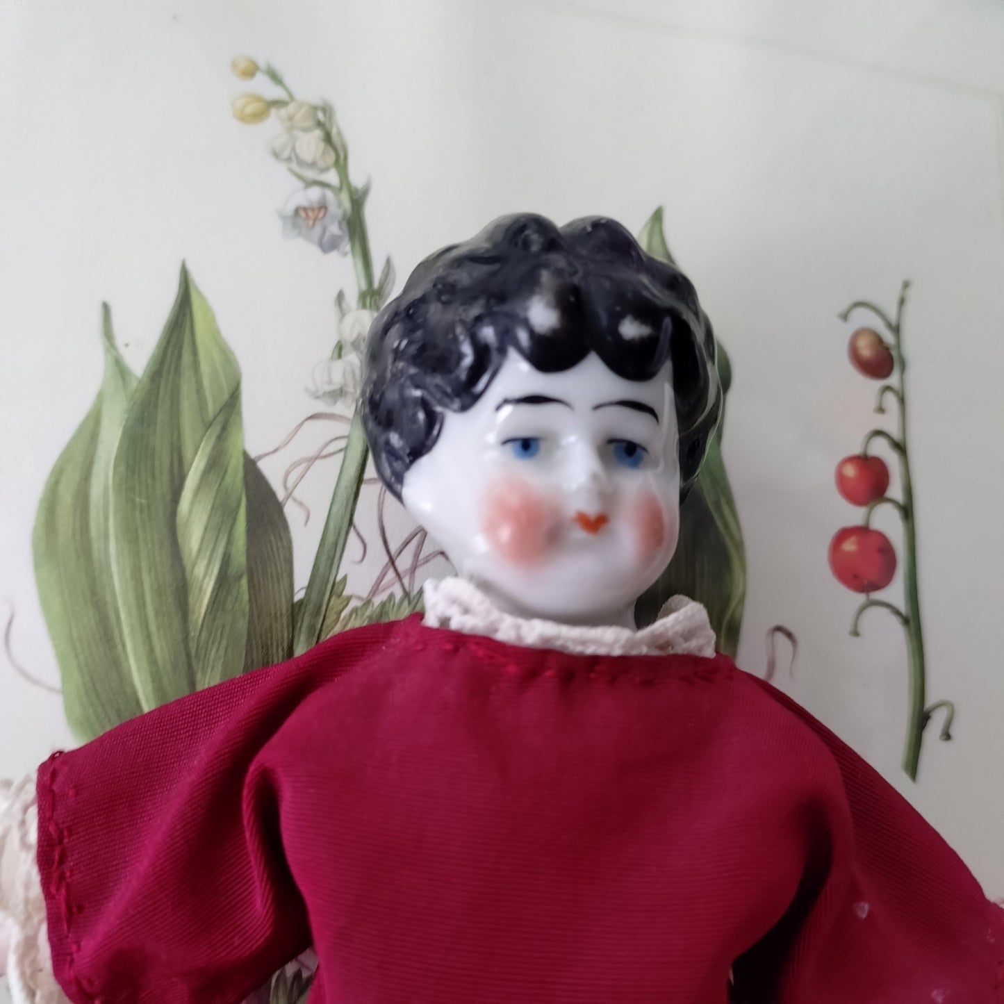 The doll in the red dress is approximately 21 cm high and likely dates to around 1900.