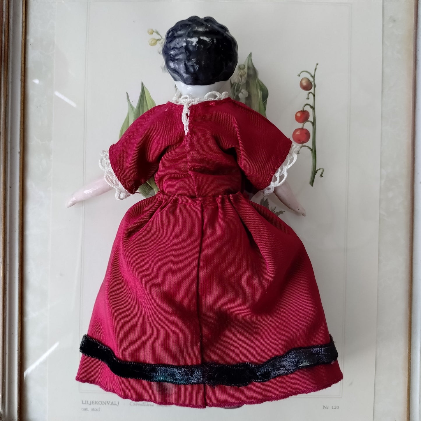 The doll in the red dress is approximately 21 cm high and likely dates to around 1900.