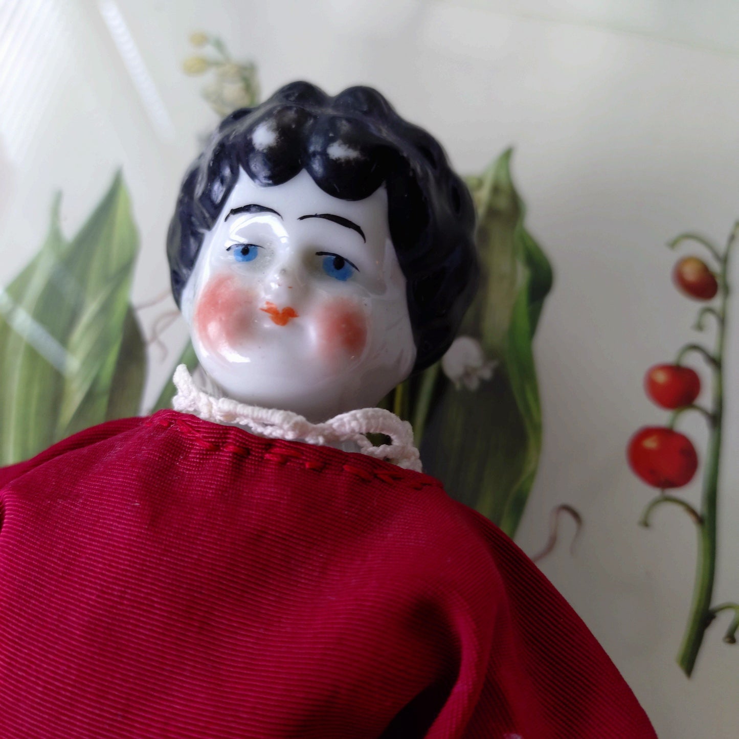The doll in the red dress is approximately 21 cm high and likely dates to around 1900.