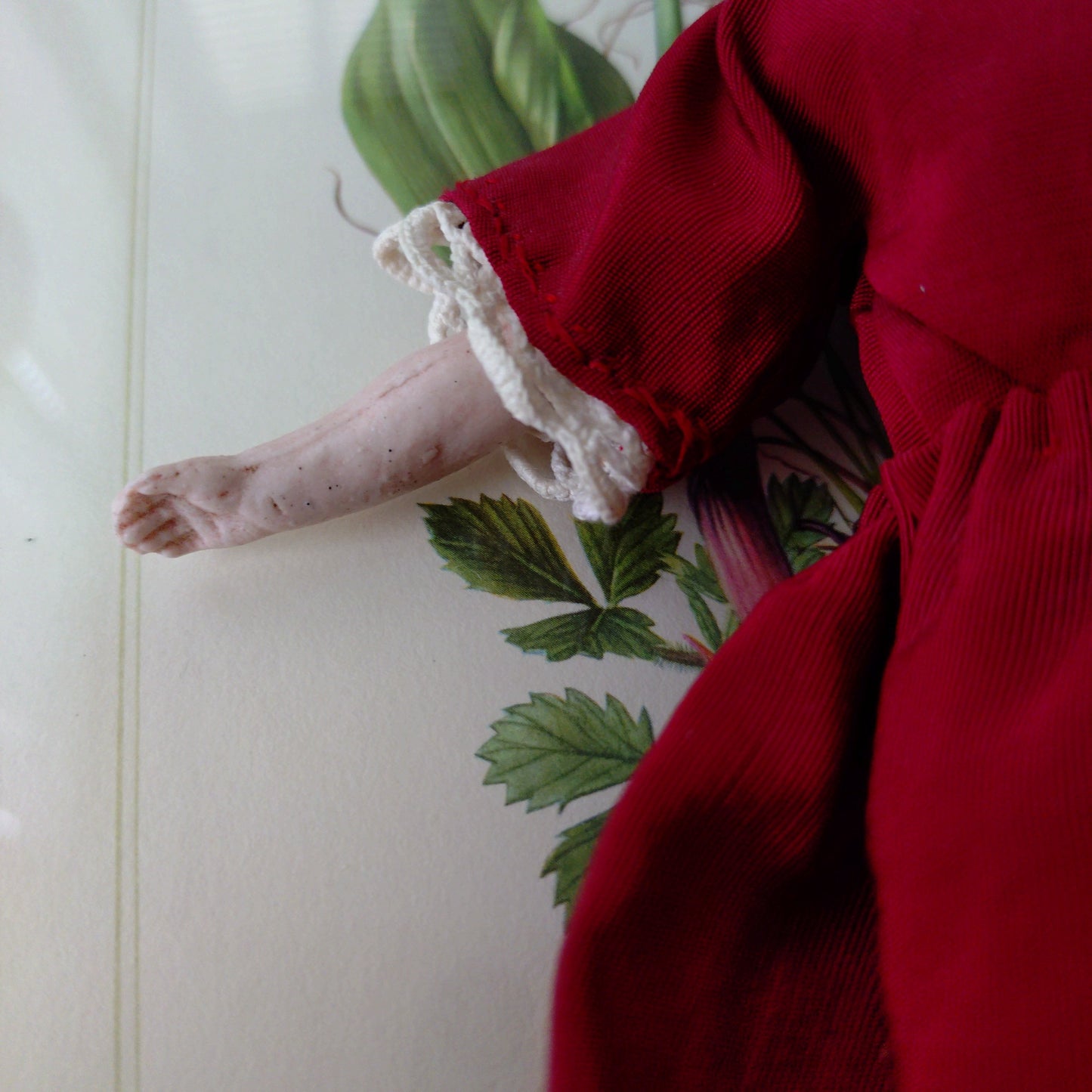 The doll in the red dress is approximately 21 cm high and likely dates to around 1900.