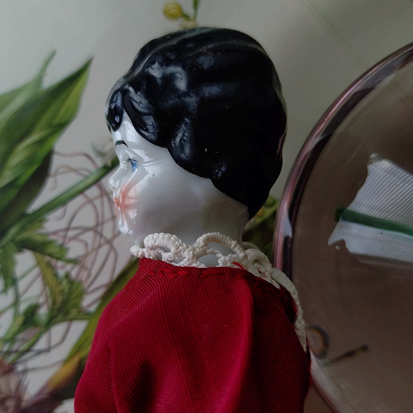 The doll in the red dress is approximately 21 cm high and likely dates to around 1900.