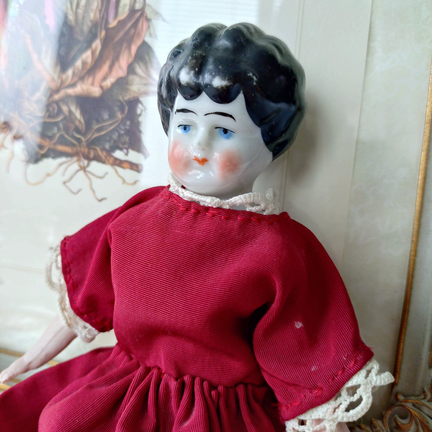 The doll in the red dress is approximately 21 cm high and likely dates to around 1900.