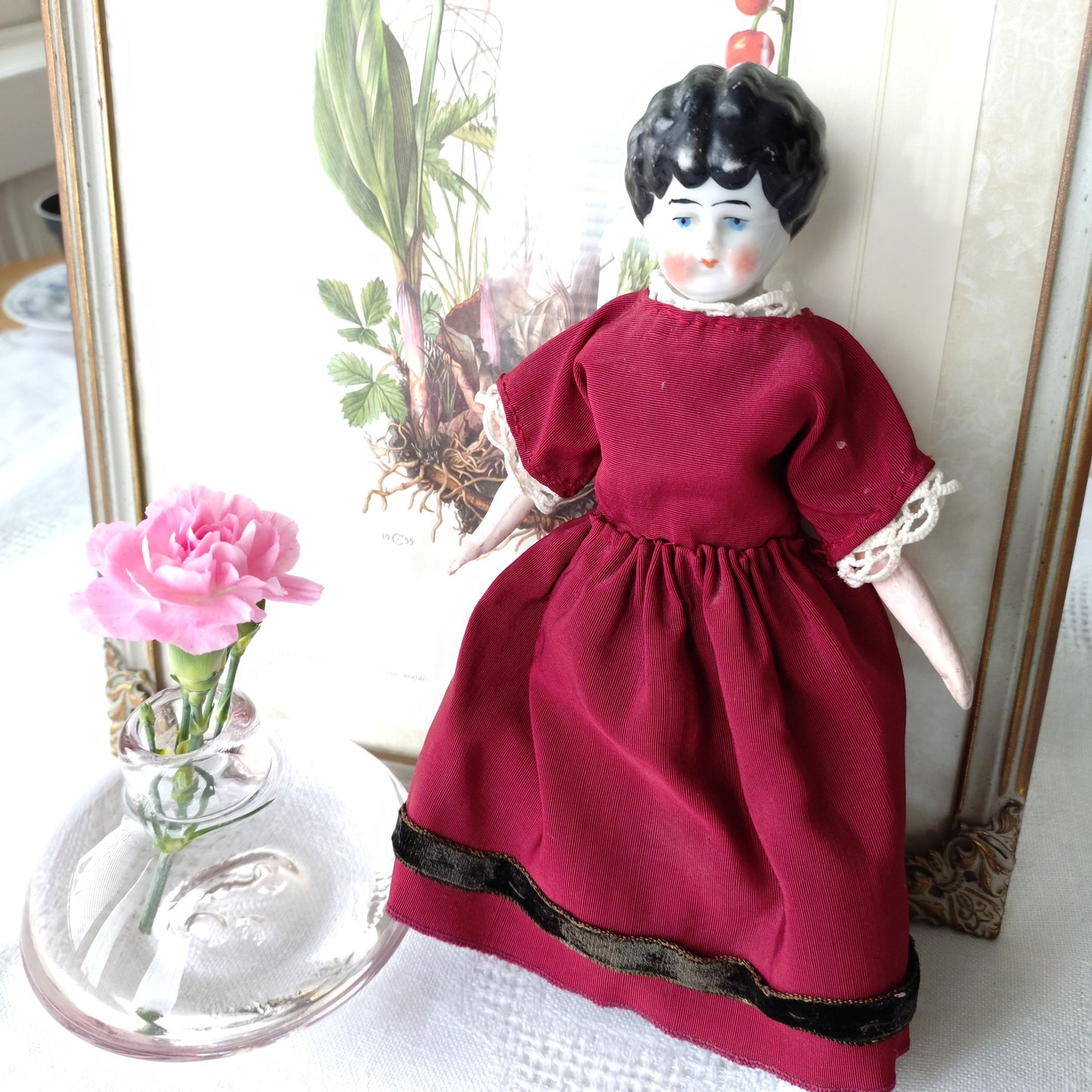 The doll in the red dress is approximately 21 cm high and likely dates to around 1900.
