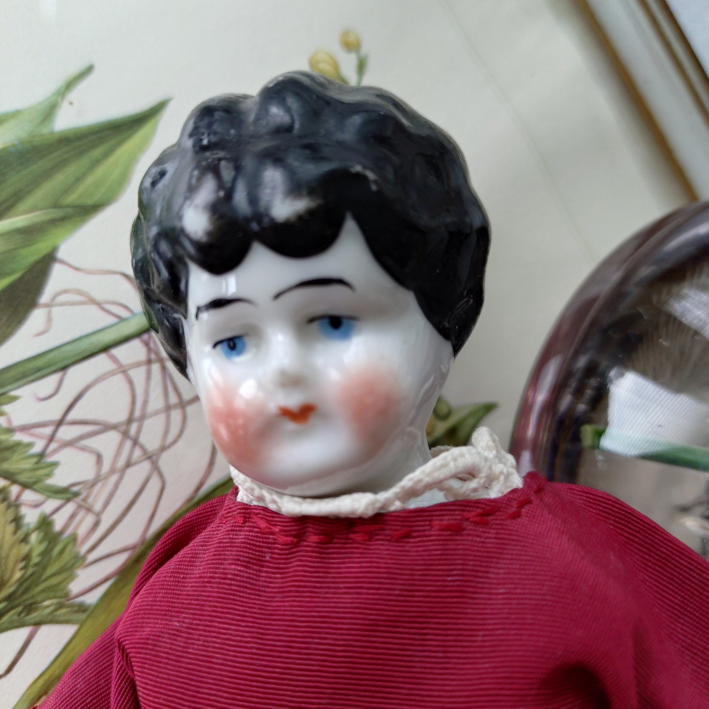 The doll in the red dress is approximately 21 cm high and likely dates to around 1900.