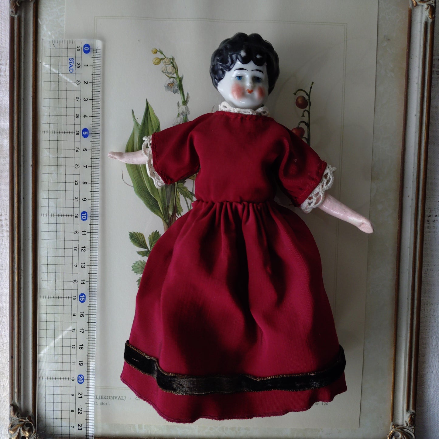 The doll in the red dress is approximately 21 cm high and likely dates to around 1900.